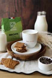 Organic hazelnut and chocolate cookies, 100g. Cookies made with organic hazelnuts and chocolate. Includes a glass of milk and additional cookies on a wooden tray.
