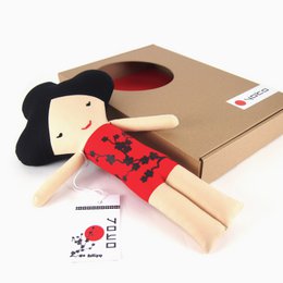 "A Japanese-style baby doll with a red and black patterned outfit and a wooden tag that says 'Hajimemashite, yoroshiku desu' in Japanese."