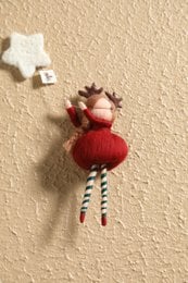 Red felt ornament with striped legs and a star-shaped headdress, hanging from a wall.
