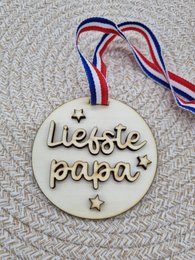 "Wooden medal-shaped ornament with the text 'Liefste papa' (Dearest Dad) and star decorations, attached to a red, white, and blue ribbon."