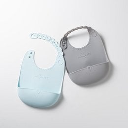 Two bibs in different colors - grey/aqua and light blue. The bibs have a simple, minimalist design with a snap closure at the neck.
