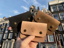 Handmade leather wallet in brown, black, and natural colors. Features a simple, minimalist design with metal hardware accents.