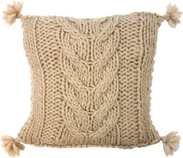 Cozy knitted pillow cover in a beige color with a textured cable pattern and tasseled corners, suitable for a rustic or farmhouse-style home decor.