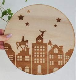 A round wooden wall decoration featuring a silhouette of a city skyline with houses, buildings, and a deer against a starry night sky background. The product is available in various sizes ranging from 15 cm to 30 cm in diameter.
