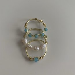 This statement ring features a large pearl surrounded by a twisted gold band with turquoise accents, creating a unique and eye-catching design. The ring is available in gold or silver with various crystal, pearl, or turquoise stone options.