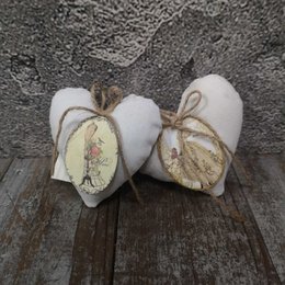 Two heart-shaped pendants with floral designs, made of white and beige materials, suspended on a wooden surface.
