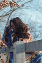 A colorful, patterned poncho with a triangular design in shades of blue, orange, and yellow. The poncho has fringed edges and appears to be made of a soft, woven material.