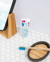 Cherry-flavored, natural, and vegan toothpaste in a tube with a wooden toothbrush holder and hexagonal tile background.
