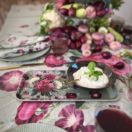 Floral patterned tablecloth with pink and purple flowers, plates, and bowls on a table setting. The tablecloth appears to be extra length and the overall style is a blossom garden theme.