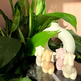 A tall, round, off-white candle in the shape of a woman's torso. The candle is made from vegan soy wax and is available in several neutral color variants including pearl, cream, peach, rosy, dove, and dusky.