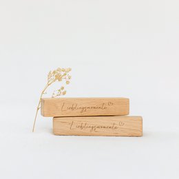  A set of two wooden card holders in a linen bag, with the text "Favorite Moments" printed on the wooden pieces. The set is presented on a plain white background, with some dried flowers or plants visible.