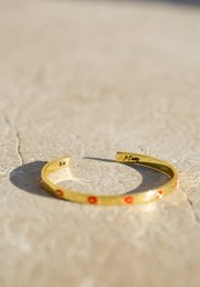 Gold-toned bangle bracelet with heart-shaped charm and red accent beads.