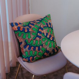 Colorful, patterned cushion with abstract, organic shapes in green, blue, and orange. Decorative accent piece for the home.