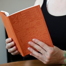 A notebook with an embossed city map design in shades of orange. The notebook has a hardcover and appears to be part of a collection or series called "Amsterdam".