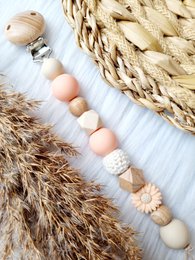 Pacifier clip with daisy and peach-colored beads. Soft, textured design with natural materials.