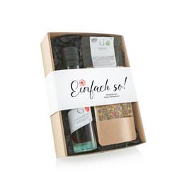 A gift set containing a red bottle, a jar of herbs, and a jar of oil, packaged in a wooden box with a white label that says "Einfach so".