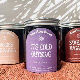 A round, tall candle in a glass jar with a silver lid. The candle is labeled "It's Cold Outside" and has a cozy, winter-themed design.