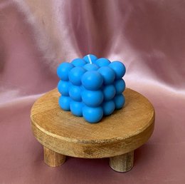 A round, tall, blue candle made of wax, displayed on a wooden stand.