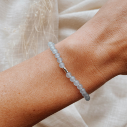 A delicate blue chalcedony bracelet with a calming, natural aesthetic. The bracelet features a simple, minimalist design with a single stone bead on a neutral-colored cord.