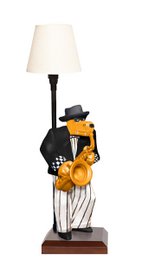  A modern desk lamp with a black base and a white lamp shade. The lamp features a decorative figurine of a jazz musician playing a saxophone.
