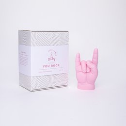 A pink, rock-shaped candle in a white box with a graphic design. The candle is in the shape of a hand making the "rock on" hand gesture, in a vibrant pink color.