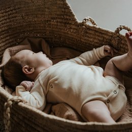 Soft, natural-colored merino wool romper with long sleeves for a newborn baby. Wrap-over design for easy dressing.
