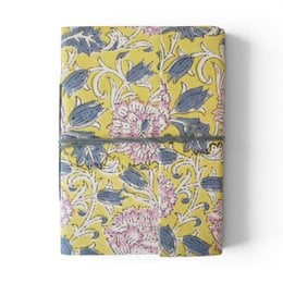 Notebook covered with violet printed fabric featuring floral patterns and designs.
The notebook is covered in a violet-colored printed fabric with a floral pattern. The design includes stylized flowers and leaves in shades of purple, blue, and pink. The fabric has a textured, embroidered-like appearance, adding visual interest to the notebook cover.