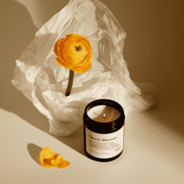 Tall, round, orange-colored candle with a floral scent. Made of natural wax and presented in a dark glass container.