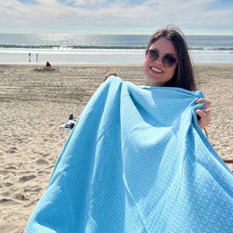  Large, soft, 100% cotton beach towel in a light blue color with a textured waffle pattern. Ideal for drying off after swimming or sunbathing on the beach.