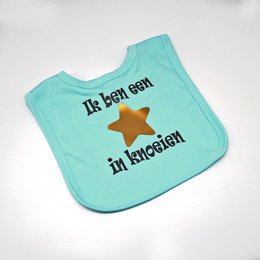 Mint green bib with a star design and the text "It's been ash in ketchup" printed on it. The bib appears to be made of a soft, absorbent material suitable for catching drips and spills during feeding.