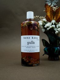 Amber-colored body massage oil in a glass bottle, with a label that says "Soul Oil (body massage)". The oil is surrounded by dried flowers and a decorative glass jar.