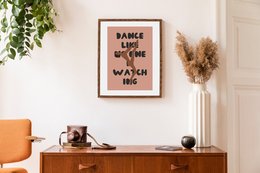 Framed wall art with the text "Dance Like No One Is Watching" in a bold, stylized font against a pink background. The artwork features a silhouetted figure dancing, capturing the playful and carefree spirit of the message.