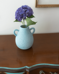 Tall, round blue vase with purple hydrangea flowers.