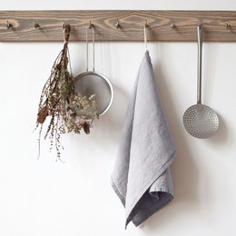 Light grey linen kitchen towel with hanging dried flowers and kitchen utensils.