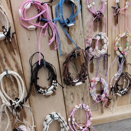  Assorted display bracelets in various colors and styles, including braided, beaded, and knotted designs, presented on a wooden display board.