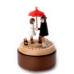 A wooden music box with a red umbrella-shaped top, featuring two figurines of a man and a woman standing under the umbrella.