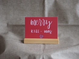 A red greeting card with the text "Merry kiss-mas" and a small heart-shaped decoration.