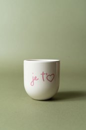 A pink ceramic mug with the text "Je t'eam" written in orange. The mug has a simple, minimalist design.