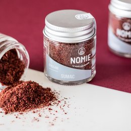 Sumac powder in a glass jar, a reddish-brown spice with a tangy, lemony flavor. Suitable for seasoning meats, vegetables, and salads.