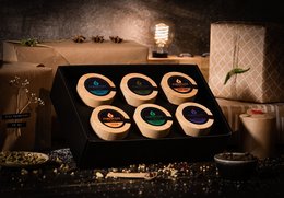 A selection box of various spices and seasonings, including round, dark-colored spice containers arranged in a grid pattern on a wooden surface.