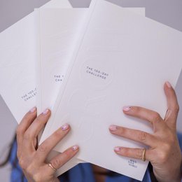A white journal titled "GROW: the 100 Days Journal Challenge" with a blue magazine cover visible in the background. The journal appears to be a self-improvement or personal growth-focused publication.