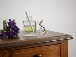 Glass reed diffuser with purple flowers, wooden cabinet, and cotton swabs. Elegant, minimalist design.