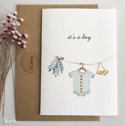 A greeting card featuring a clothesline with a romper, suitable for a baby. The card has a simple, minimalist design with a handwritten message "it's a baby" and a hanging baby outfit.