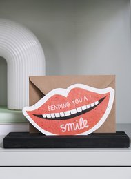 Colorful postcard with a large smile design and the text "Sending you a smile" on a wooden stand.