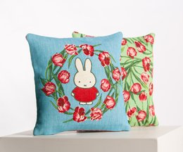 Decorative pillow featuring Miffy the rabbit surrounded by a wreath of red tulips. The pillow has a soft blue background and the design is embroidered.