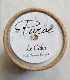 A round, white scented candle with a cork lid. The candle is labeled "Purae Le Calm" and appears to be a natural, soy-based candle.