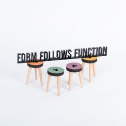 A black and white architectural quote plaque that reads "FORM FOLLOWS FUNCTION". The plaque is displayed on a desk alongside a mug, books, and other office supplies.