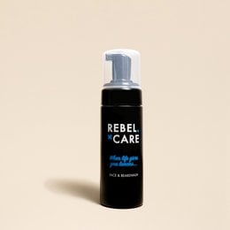 A black bottle with a white pump dispenser labeled "Rebel Care" and a lemon slice next to it. The product is a face and beard wash with a lemon scent.