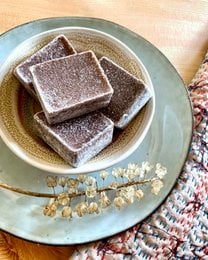 Oudh Zahra perfume block, an amber-based fragrance with a warm, earthy aroma. Rectangular shape, reddish-brown color, and textured surface.