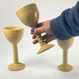  Tall, round, wooden goblets or chalices with a stem base. The goblets have a simple, minimalist design and appear to be made of a light-colored wood or material.